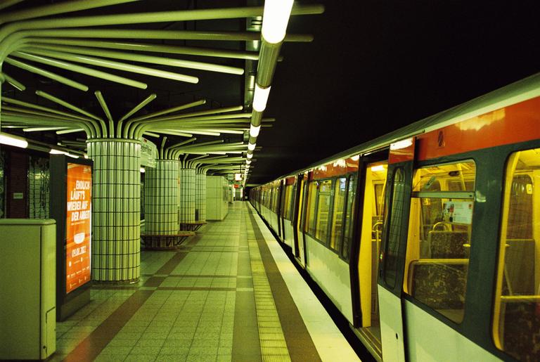 A subway train with open doors waits at a station platform with distinctive column lighting.