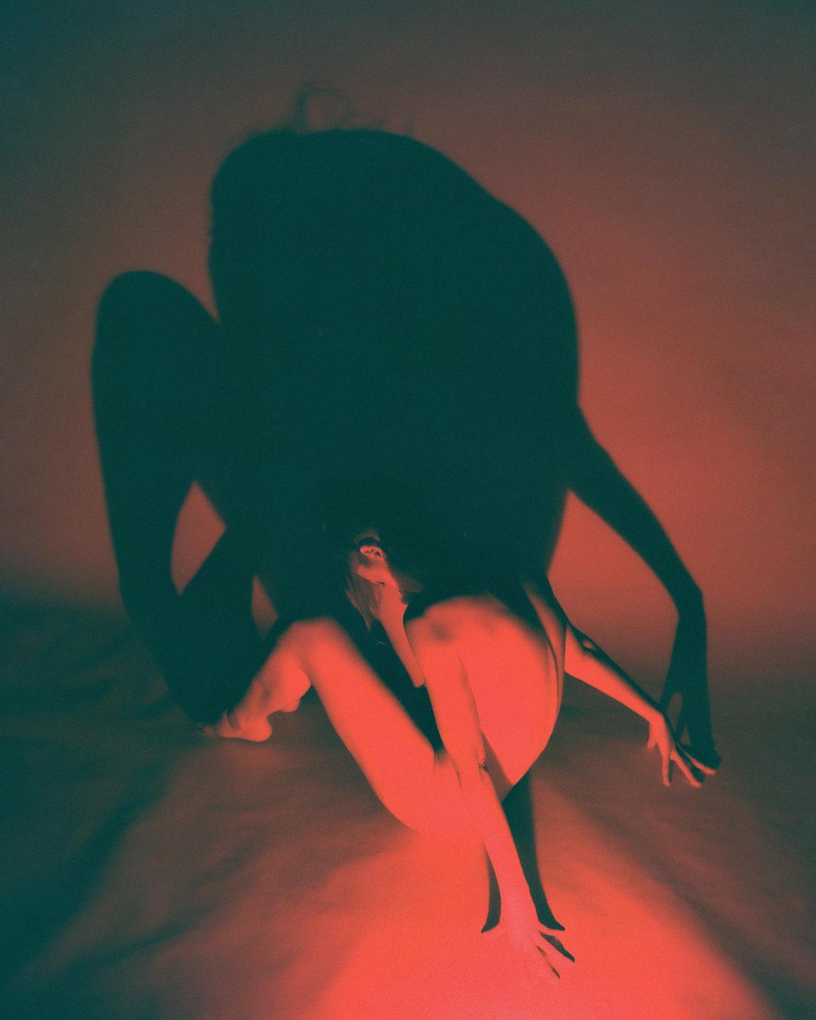 A woman sits on the floor with a large shadow behind her.