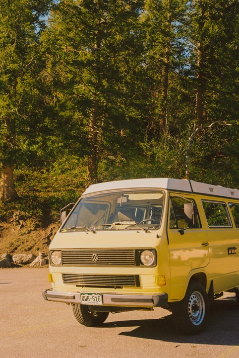 A yellow van is parked on an asphalt surface with a forest in the background.