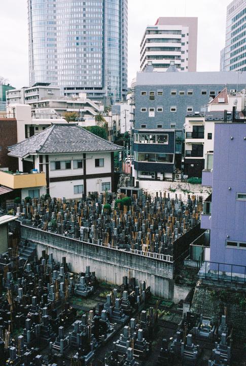 A graveyard with many tombstones and wooden markers is nestled among modern buildings in Roppongi.