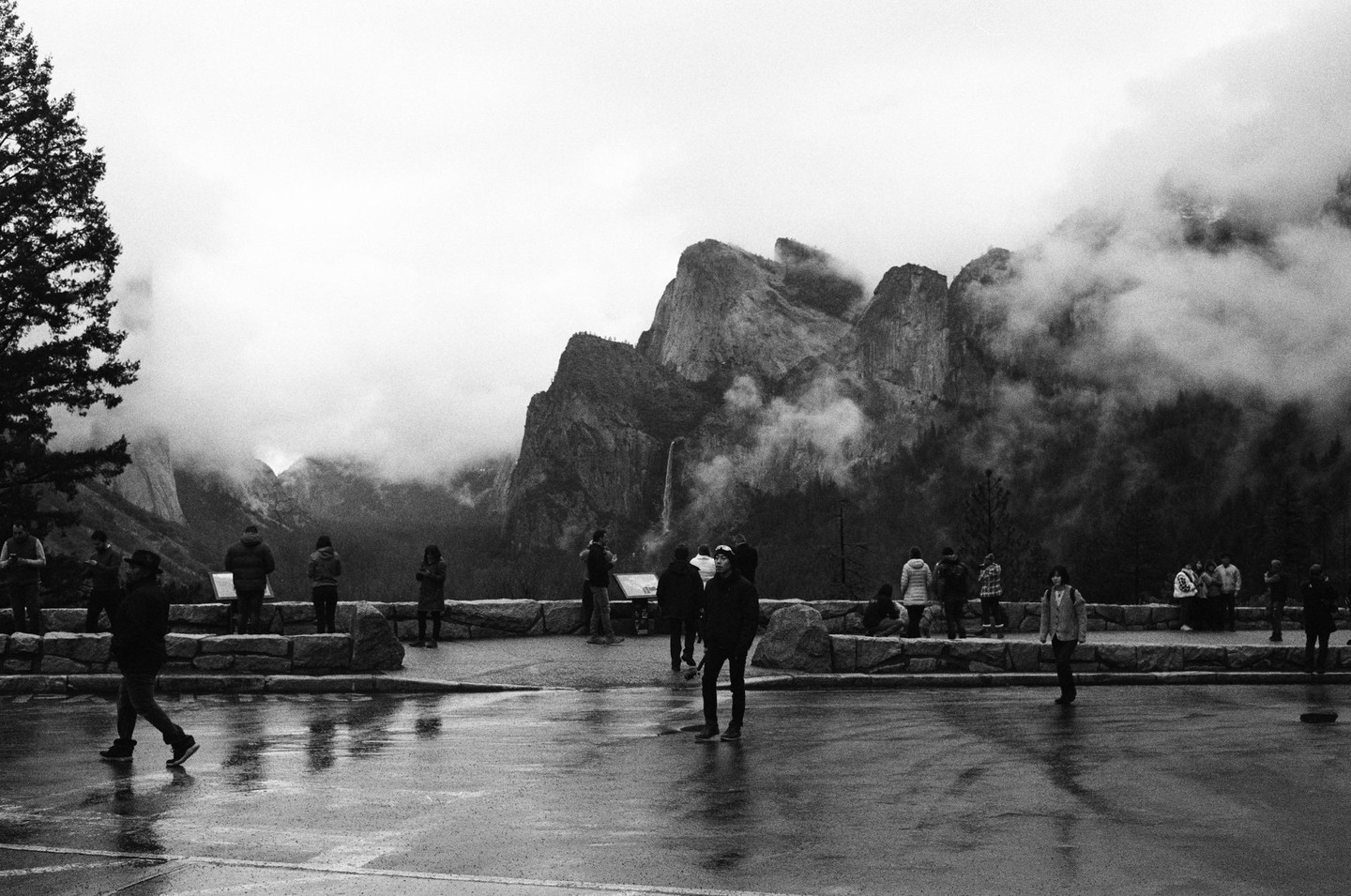 People stand on a wet overlook admiring a mountain landscape shrouded in fog.