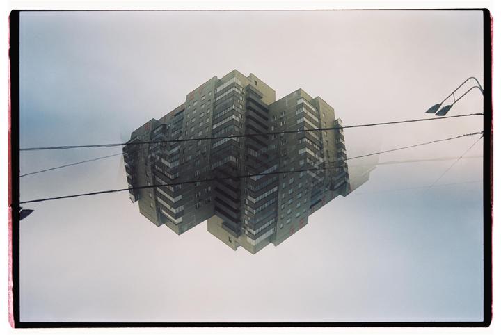 A double exposure shows a tall apartment building reflected in the sky with power lines and a street light.