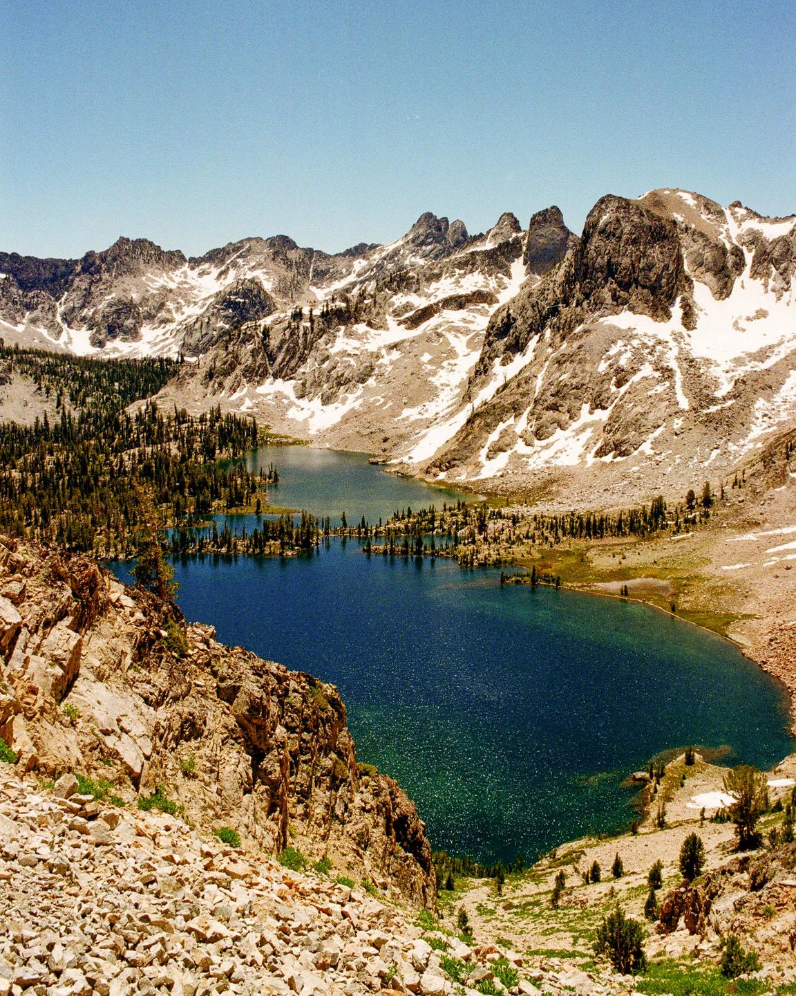 A deep blue lake is nestled among snow-capped mountains and evergreen trees.