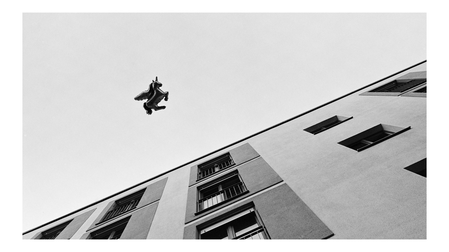 A unicorn balloon floats above a building with many windows.