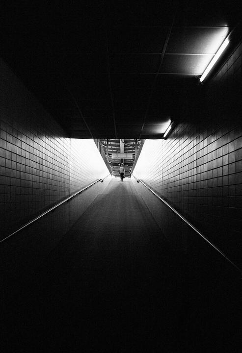 A person walks away through a dark, tiled tunnel towards a bright exit.