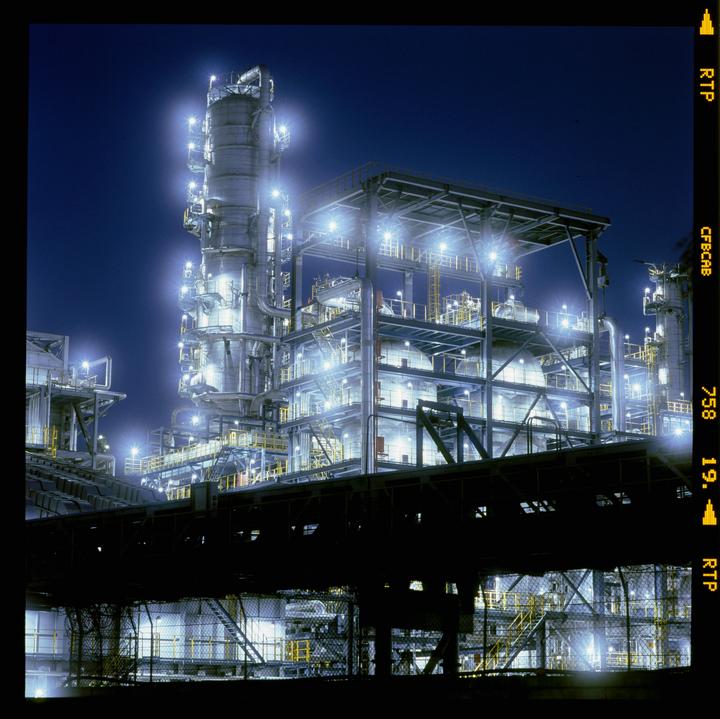 A large industrial complex with multiple levels of machinery and bright lights is shown at night.