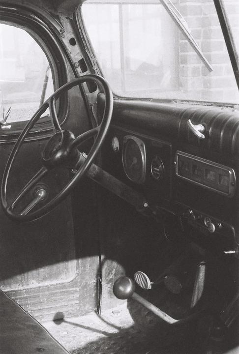 The interior of an old vehicle shows the steering wheel, dashboard, and pedals.