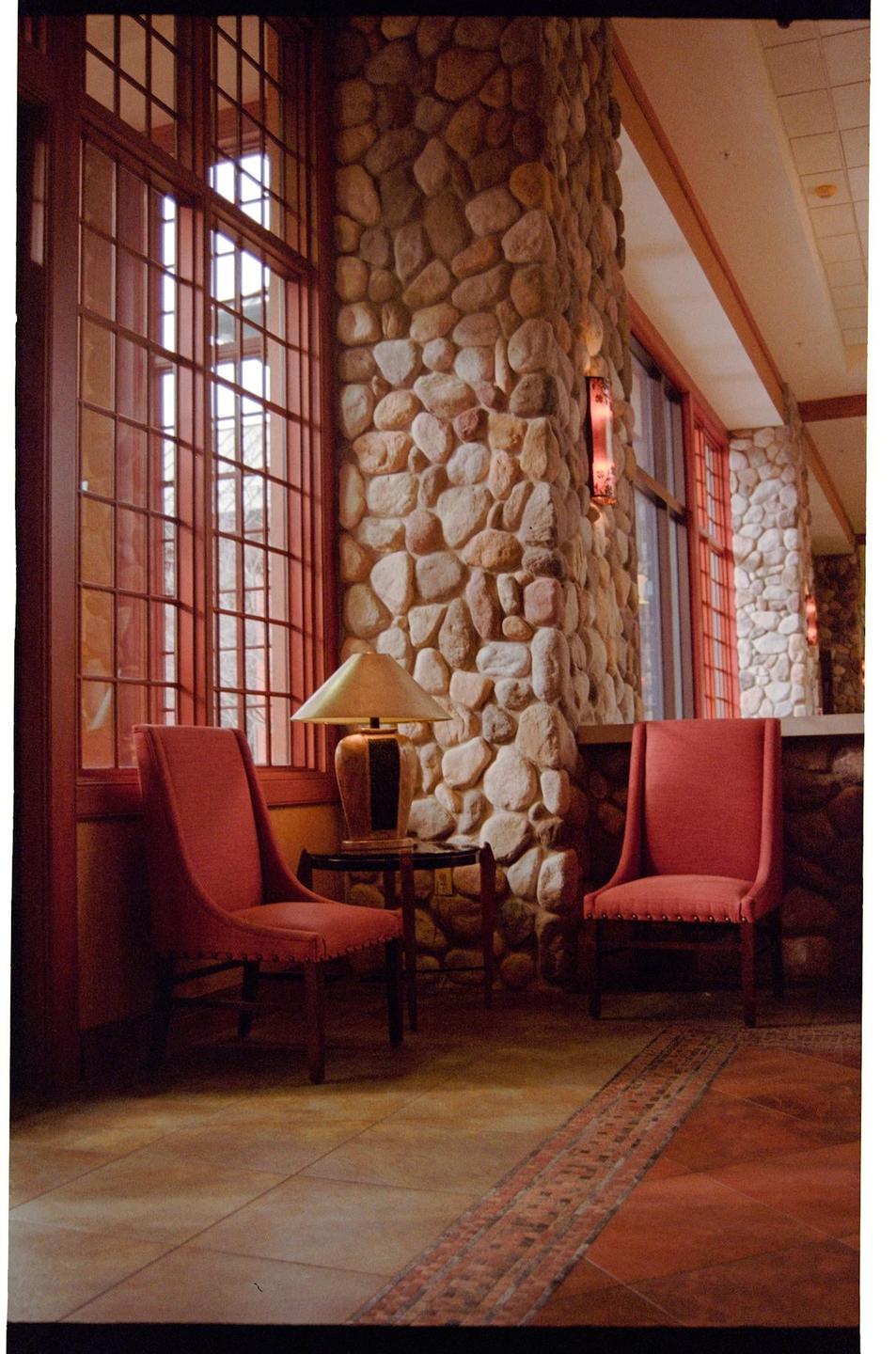 Two red chairs sit next to a stone pillar and large windows in a room with a patterned rug.