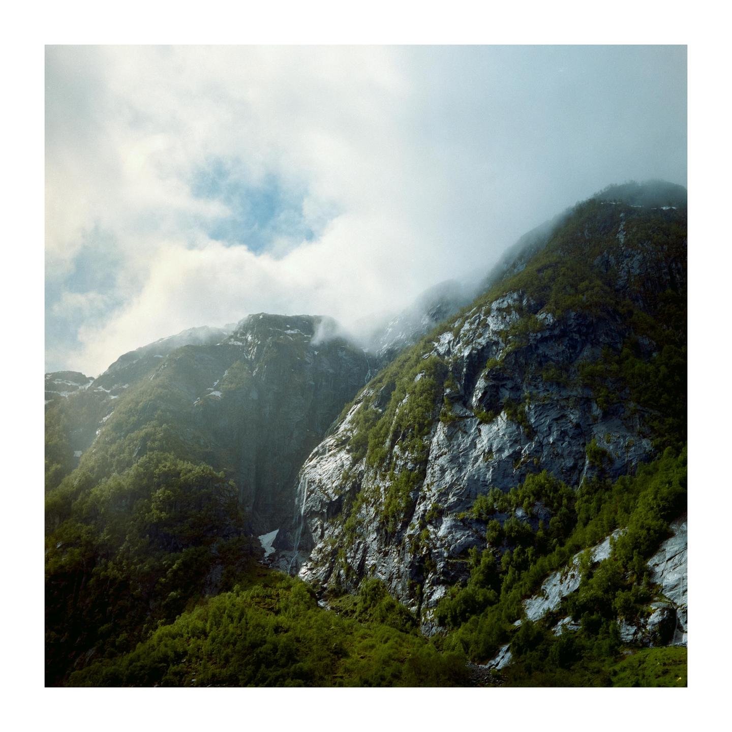 Sunlight illuminates a lush green mountain with a waterfall and mist.