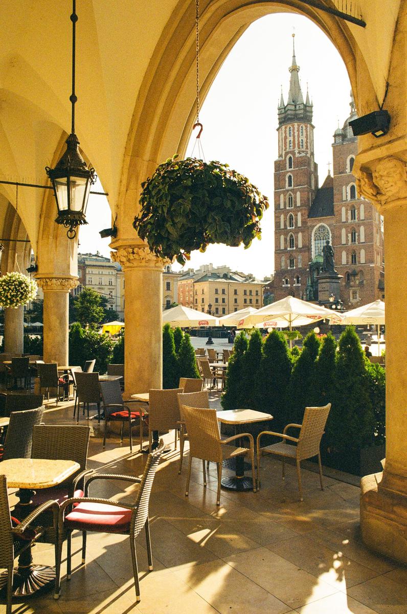 A cafe patio with tables and chairs is visible under an archway, with a church tower in the background.