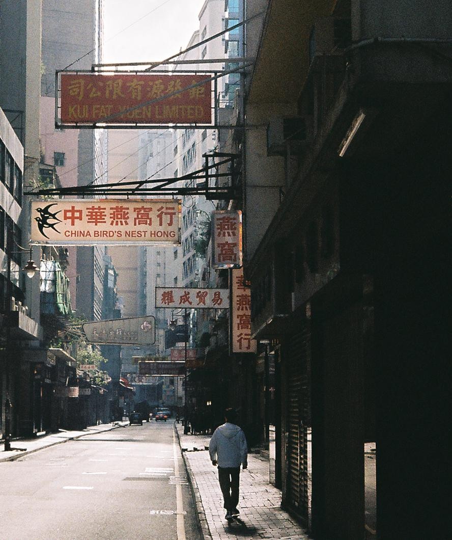 A person walks down a narrow street lined with buildings and signs in an urban setting.