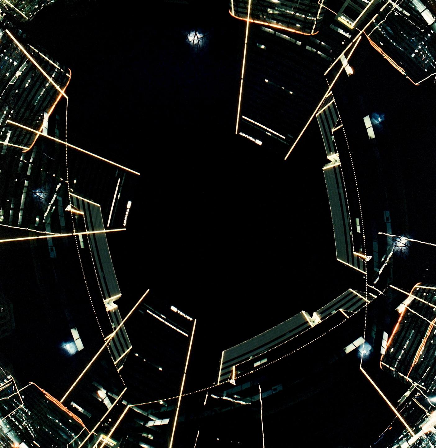 A fisheye view of city buildings at night, with illuminated windows and light trails.