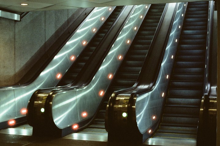 Three escalators are visible, two going up and one going down, with red and green lights on their sides.