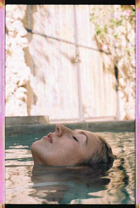 A woman floats on her back in water with her eyes closed and her face looking up.