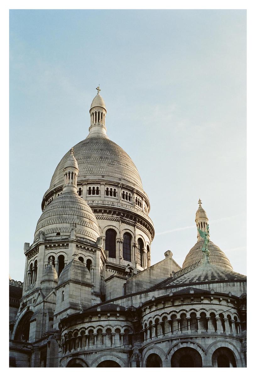 The domes and facade of the Sacré-Cœur Basilica are visible against a clear sky.