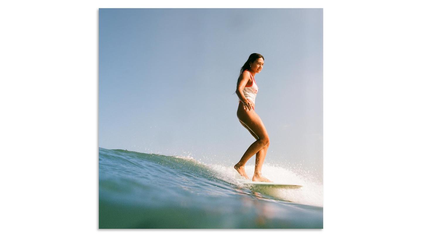 A woman in a white swimsuit surfs a wave under a clear sky.