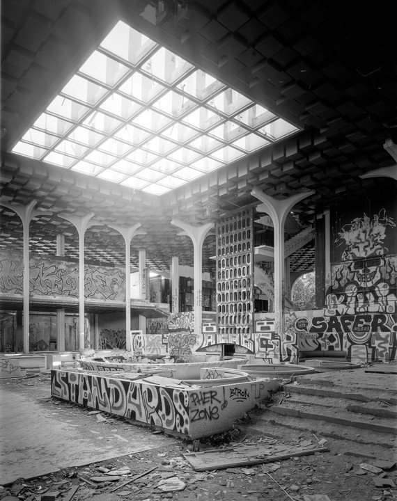 A large, abandoned building with a skylight and graffiti-covered walls and structures is shown.