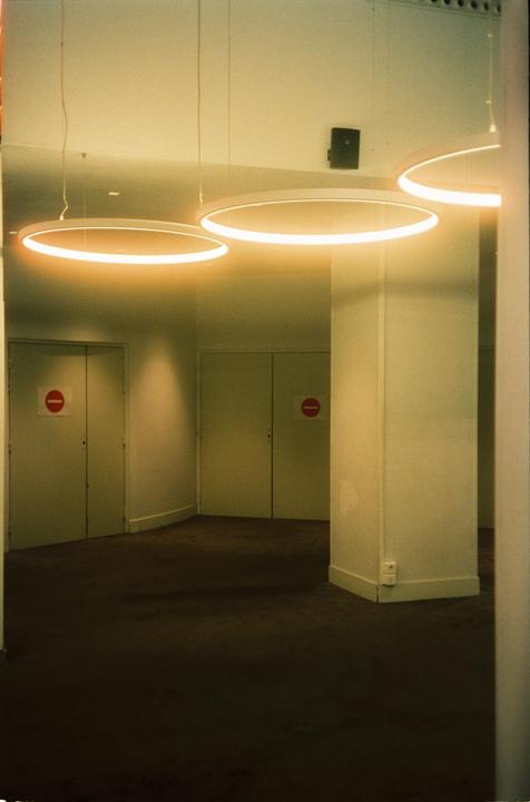 A hallway with two doors marked with red no entry signs is illuminated by three circular neon lights.