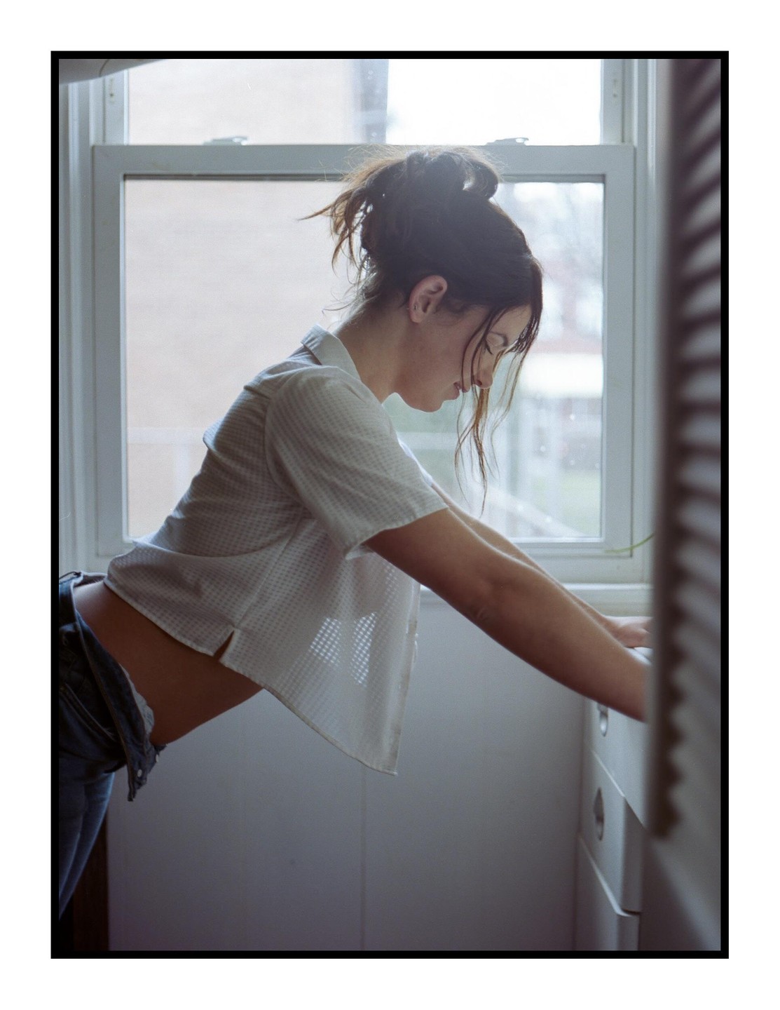 A woman leans forward with her arms on a counter in front of a window.