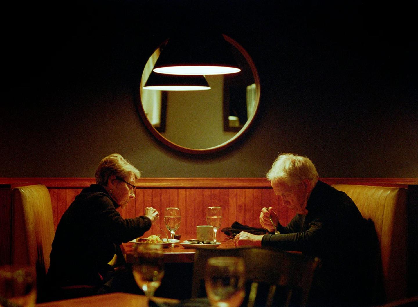 A couple sits at a restaurant table eating a meal in dim light.