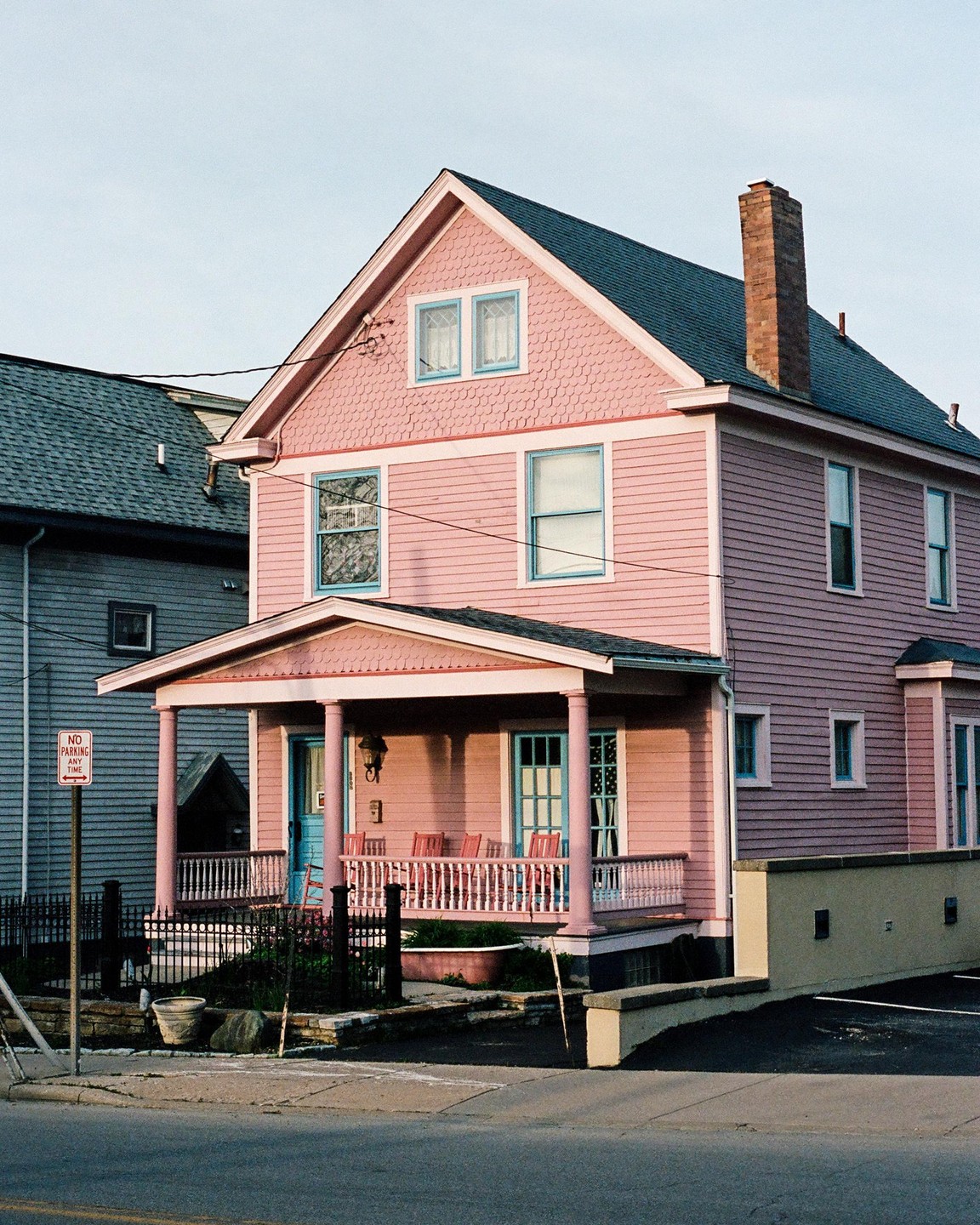 A pink house with a porch and blue trim stands next to a gray house.