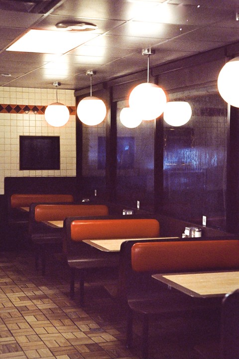 An empty diner with booths and tables is illuminated by hanging globe lights.