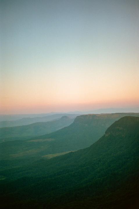 A vast landscape of rolling hills and mountains is visible under a colorful sky at dusk.