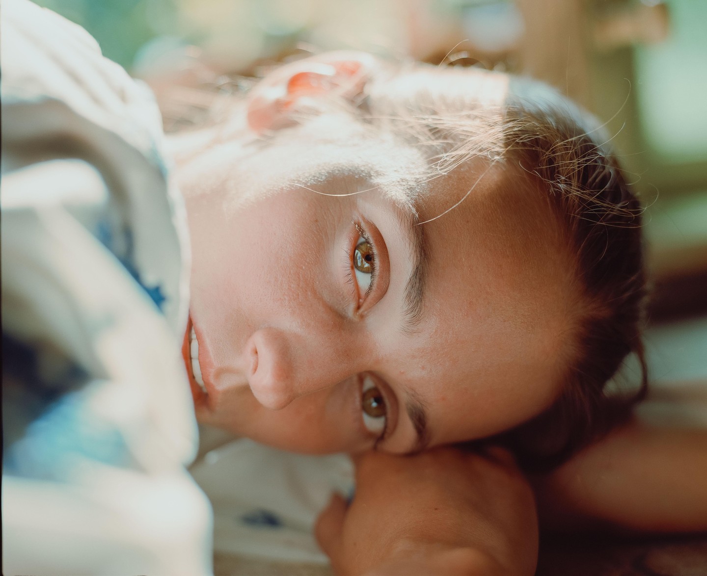 A woman with brown hair and eyes is lying down and looking at the viewer.