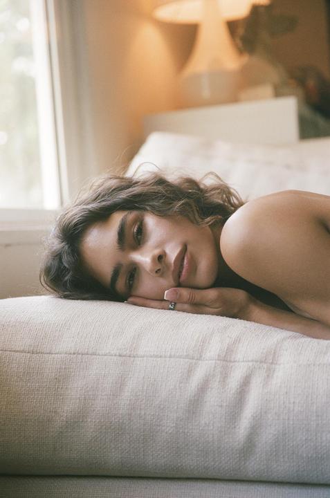 A woman with curly hair lies on a light-colored sofa, resting her head on her hand.