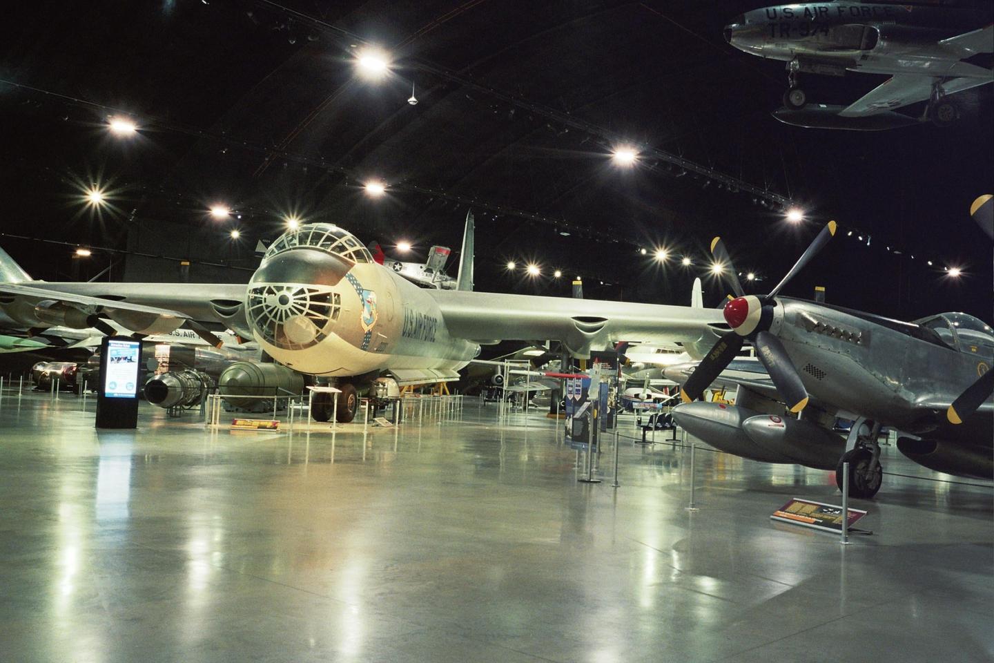 Several airplanes are displayed in a large, dimly lit hangar with bright lights on the ceiling.